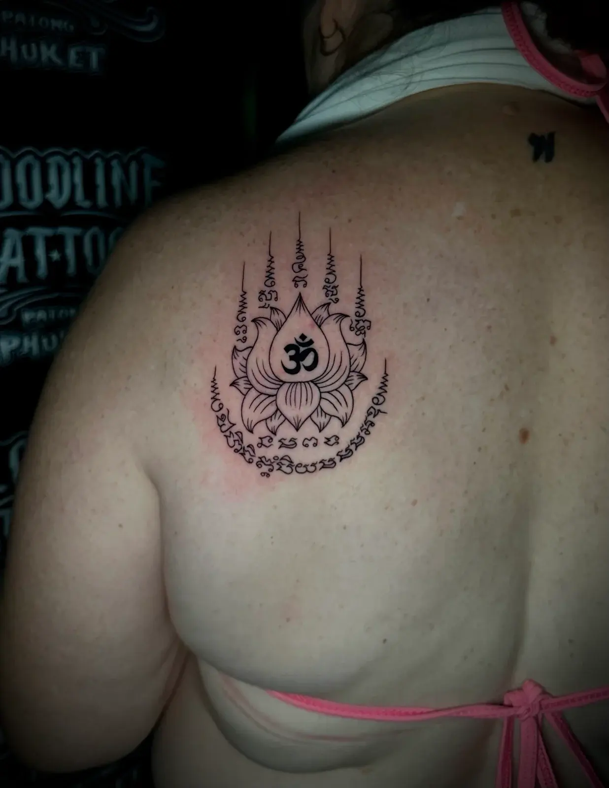 Hah Taew (Five Lines) Sak Yant with five Khom script columns, unalomes, and a central lotus flower bearing an Om symbol on the left shoulder blade at Bloodline Tattoo Phuket.