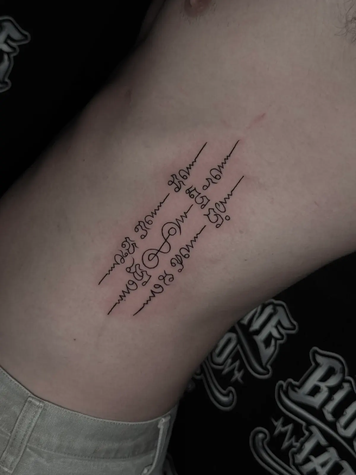 Three-line Sak Yant with diagonal Khom script columns and unalome symbols on the side ribcage at Bloodline Tattoo Phuket.
