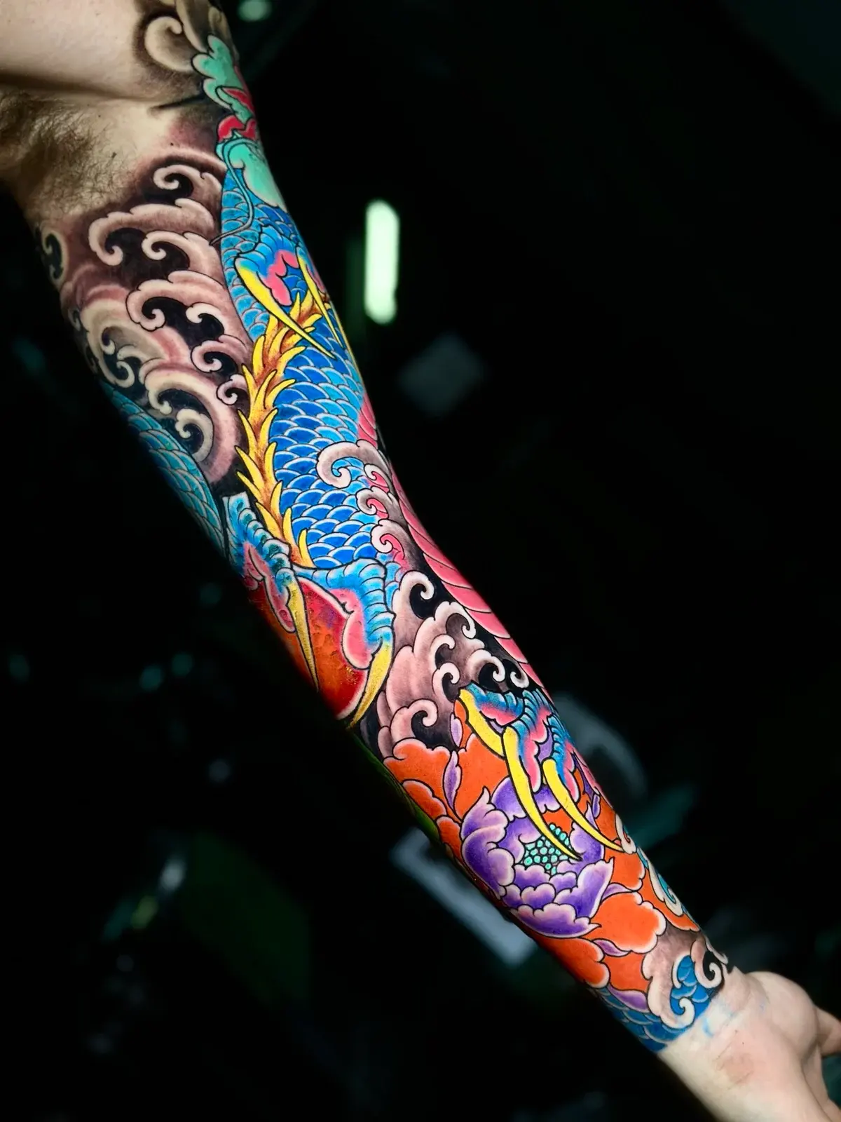 Vibrant Japanese colour sleeve featuring a coiled blue dragon, a purple peony, and traditional black wind-bar shading at Bloodline Tattoo Phuket.