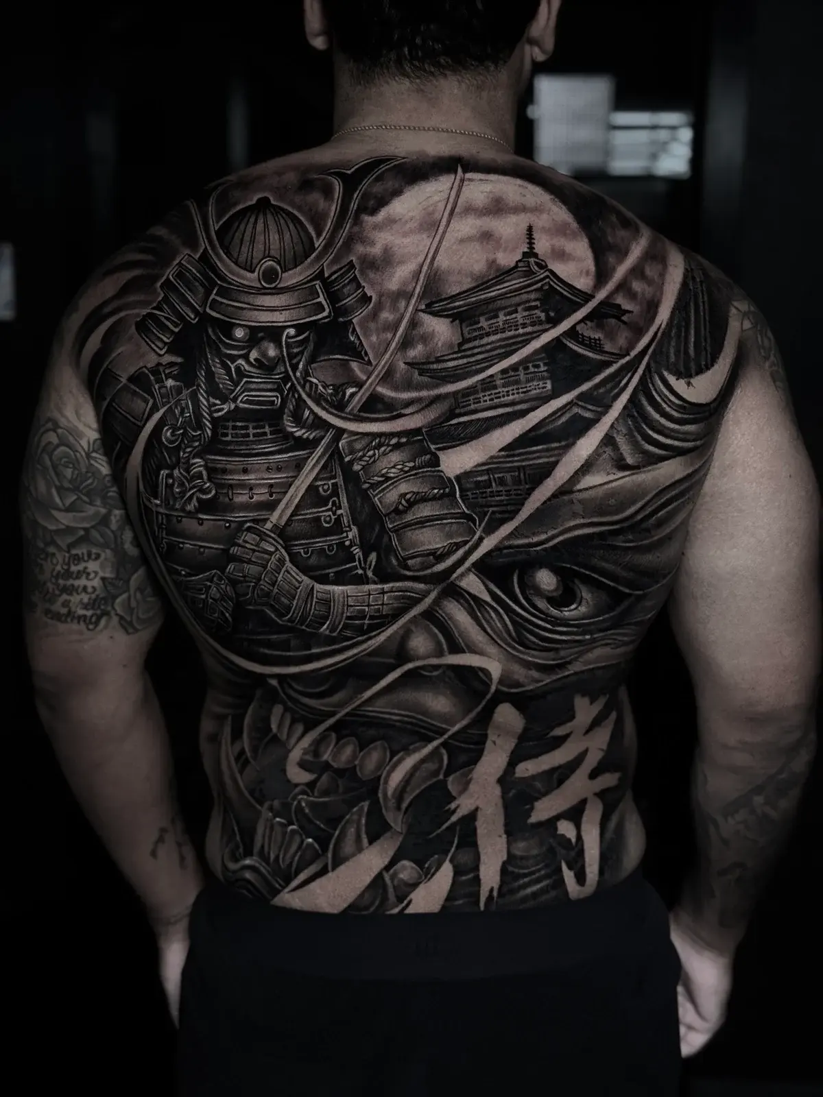 Japanese black and grey full-back piece with armored samurai, pagoda under a full moon, Hannya mask, and kanji at Bloodline Tattoo Phuket.