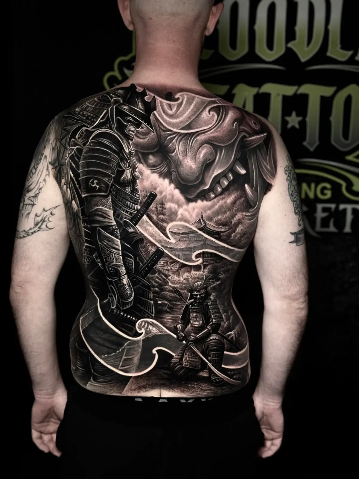 Japanese black and grey full-back with armored samurai, Hannya mask, pagoda in mist, kneeling swordsman, and flowing wind lines at Bloodline Tattoo Phuket.