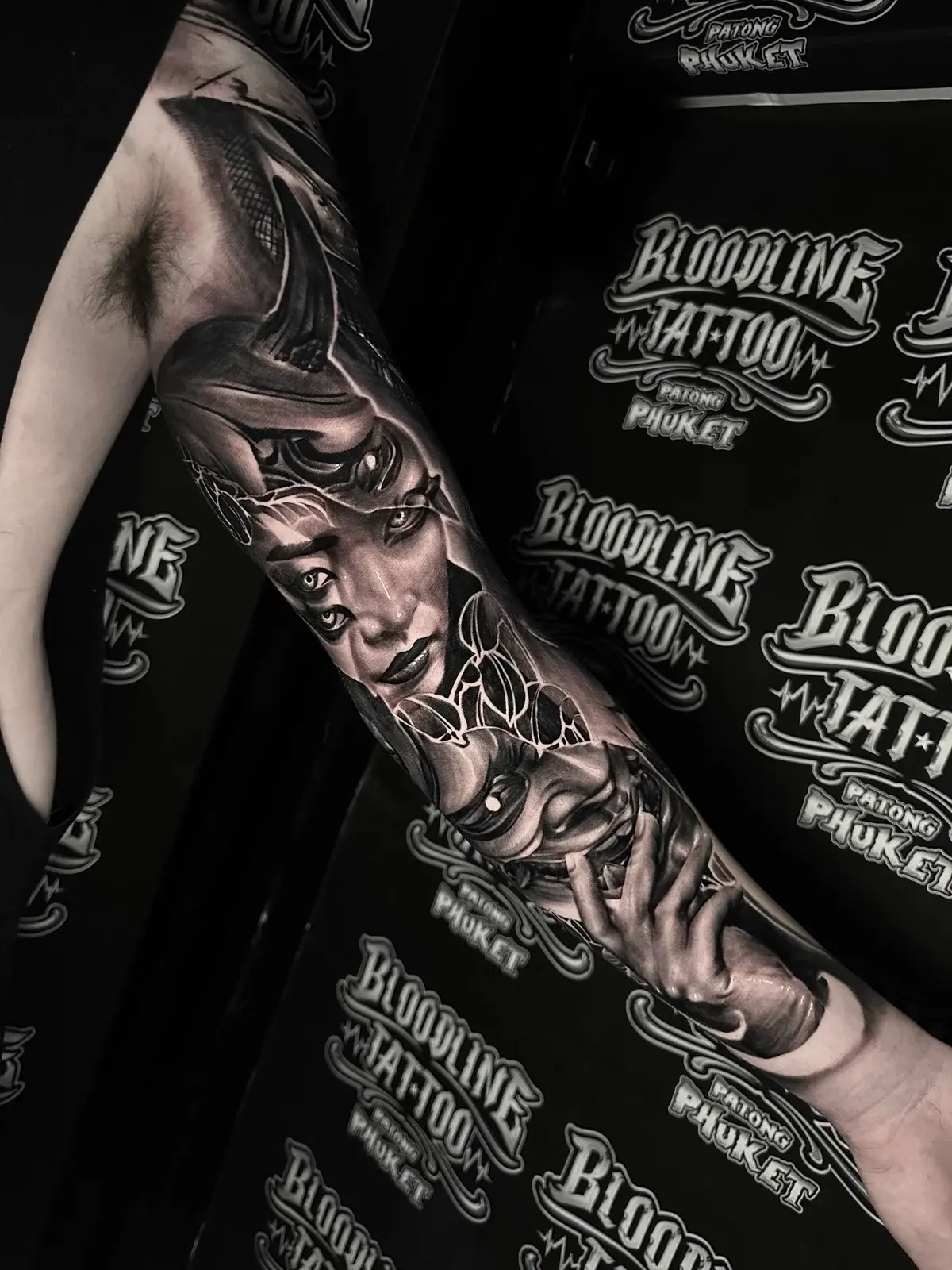 Japanese black and grey sleeve blending a four-eyed woman's portrait with Hannya horns and a hand gripping the mask's snarling jaw at Bloodline Tattoo Phuket.