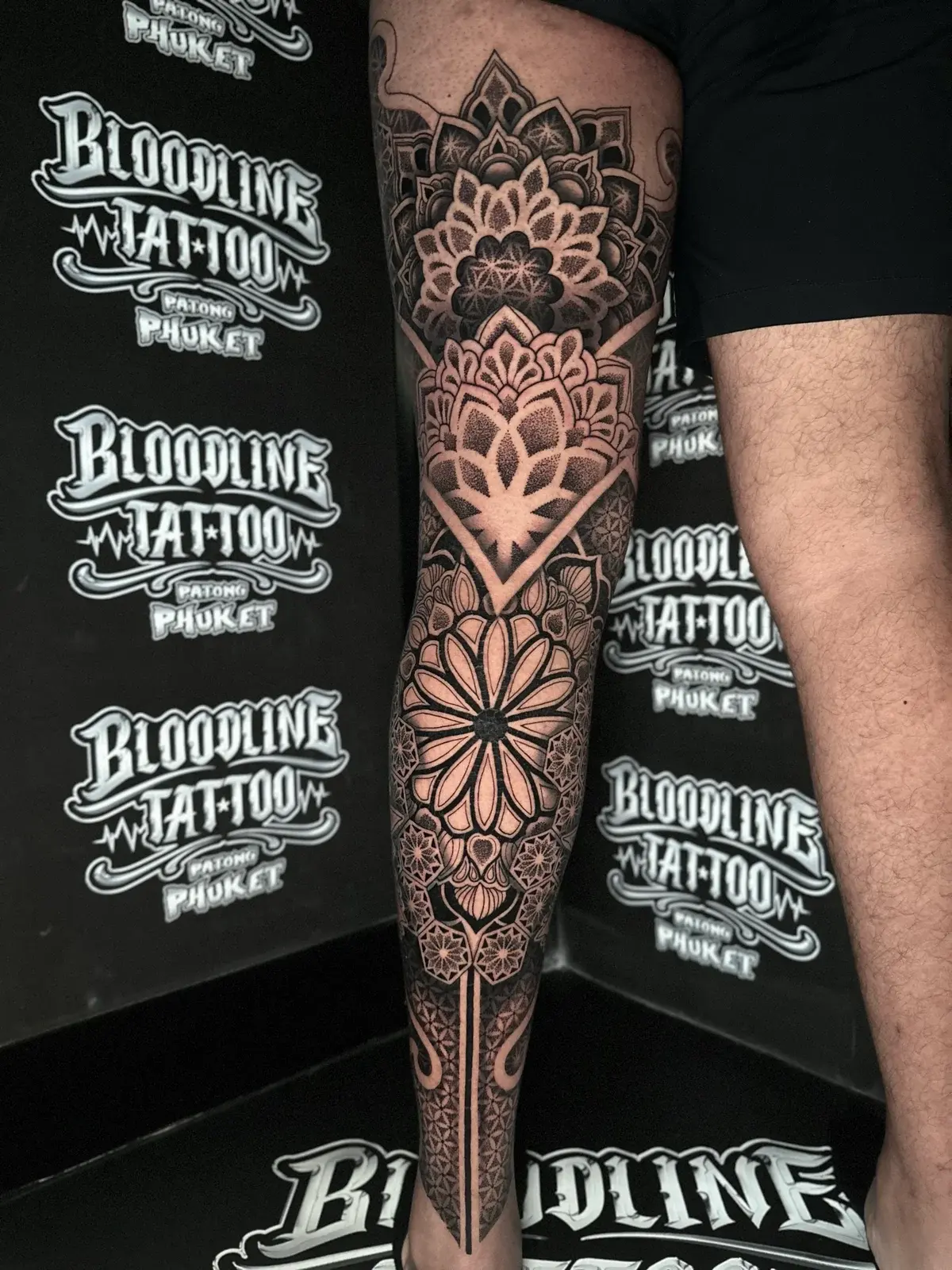 Stacked blackwork leg mandalas with a thigh lotus, a diamond-framed knee floral, and a circular shin mandala with ankle geometry at Bloodline Tattoo Phuket.