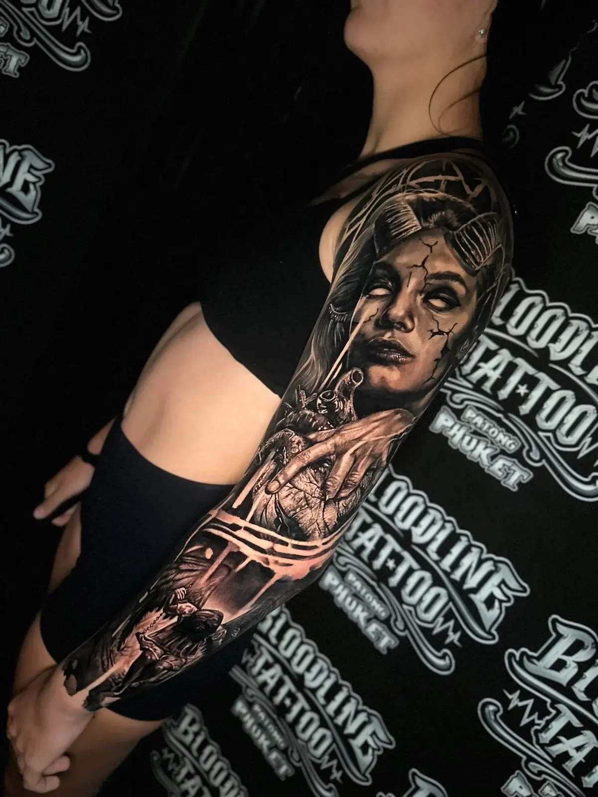 Detailed black and grey realism full sleeve tattoo featuring a horned demon woman with white eyes, anatomical heart, and hooded winged reaper at Bloodline Tattoo Phuket.
