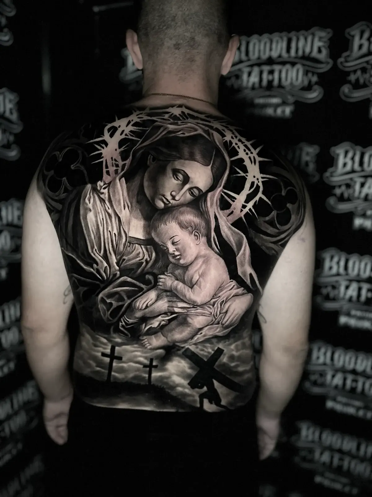 Detailed black and grey realism full back tattoo of the Virgin Mary holding the infant Jesus beneath a crown of thorns and Calvary crosses at Bloodline Tattoo Phuket.